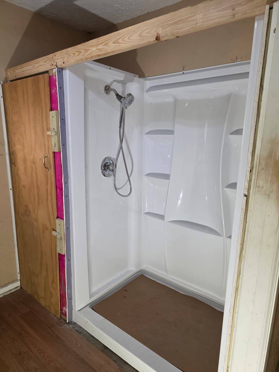 Freshly installed white acrylic shower stall with a handheld shower head and chrome valve