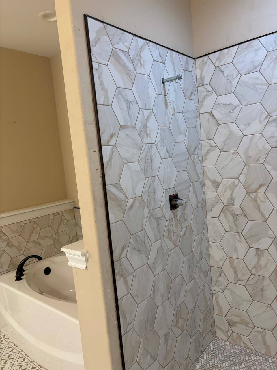 Hexagon-tiled shower wall with the shower arm and valve installed, next to a soaking tub