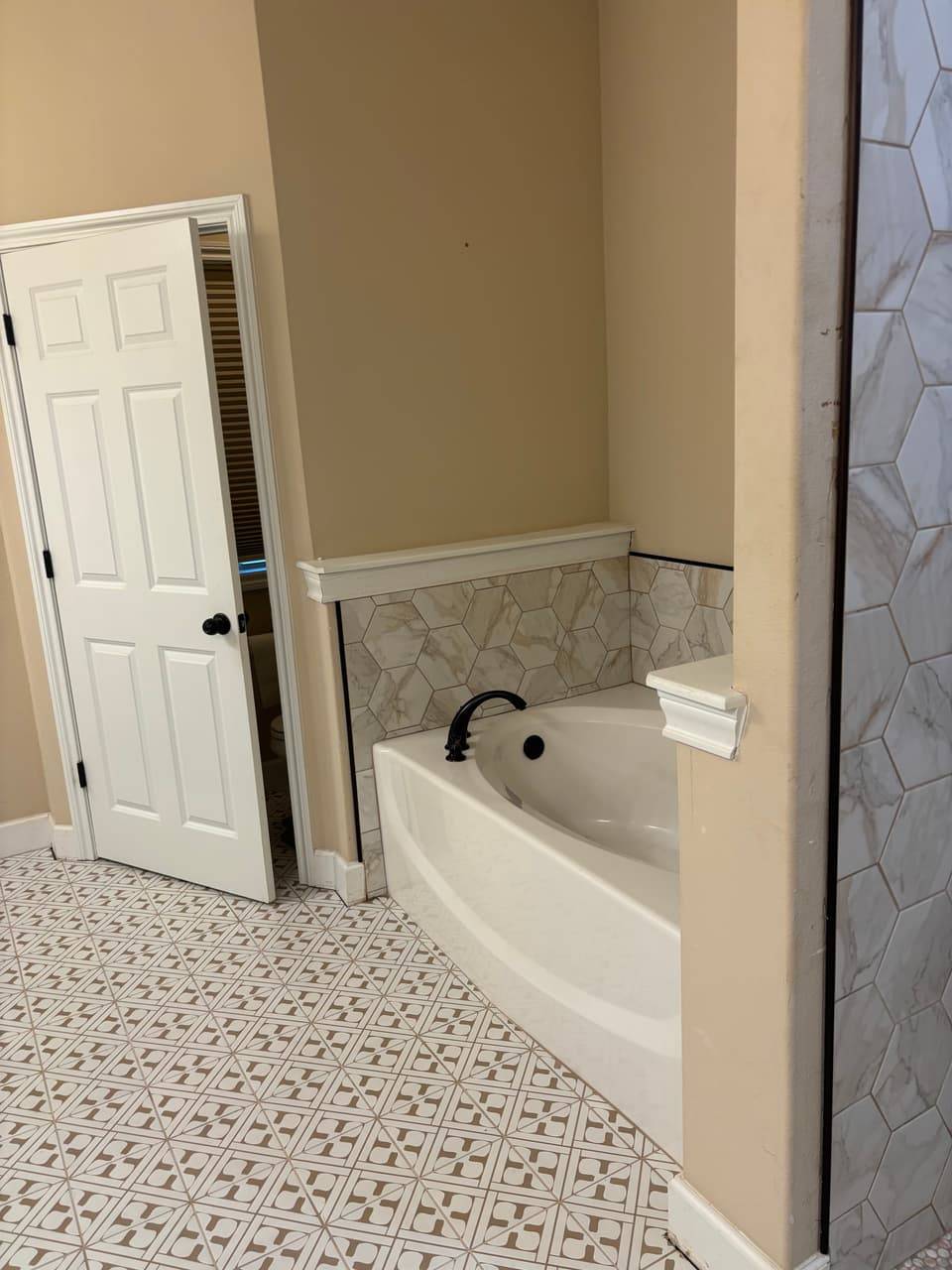 Soaking tub with a black faucet and hexagon tile surround beside a patterned tile floor